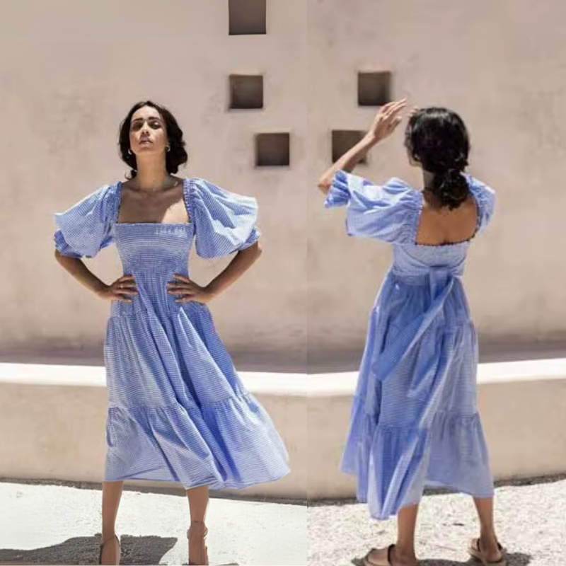 Front and back view of the Pixi Dress in light blue gingham fabric, showcasing the square neckline, puff sleeves, fitted smocked bodice, and flowing tiered midi skirt. Composite image displaying both angles of the dress against a minimalist beige background with architectural details.