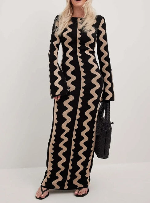 Model wears Gemini Knit Dress by ShoptheKei with a black leather tote bag and oval shaped black sunglasses. Sweater dress maxi length with long flare sleeves. Body conscious. Mod 1960's style dress with vertical wavy squiggle line patterns.