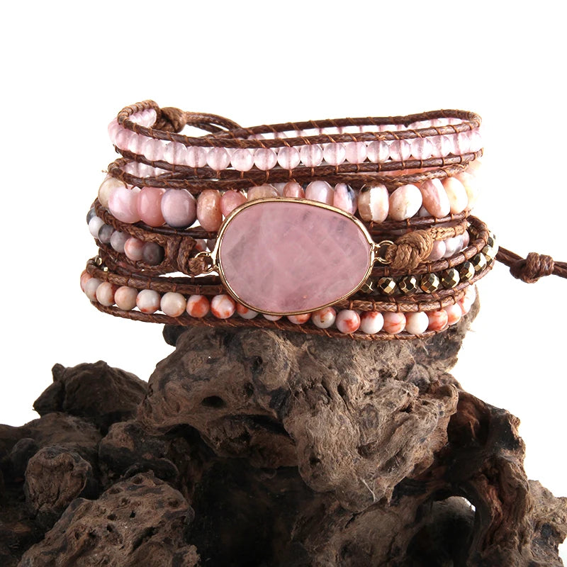 Light Pink Bohemian style wrap bracelet with a large center stone and several colorful smaller stones set in a natural cording. The bracelet rests on driftwood. Light Pink Boho Crystal Bracelet Set - Shop The Kei