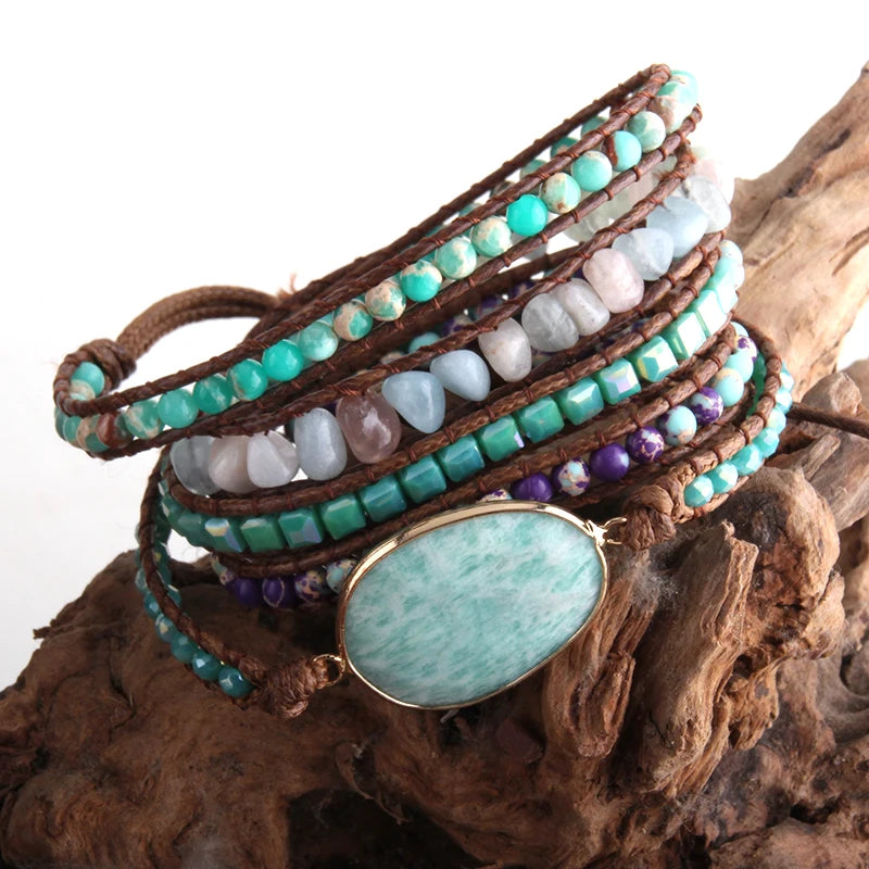 Energeticly bright and fresh light blues with purple and earthy tone Bohemian style wrap bracelet with a large center stone and several colorful smaller stones set in a natural cording. The bracelet rests on driftwood. Boho Crystal Wrap Bracelet at Shop the Kei