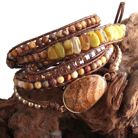 Golden sunshine yellows and earthy tone Bohemian style wrap bracelet with a large center stone and several colorful smaller stones set in a natural cording. The bracelet rests on driftwood. Boho Crystal Wrap Bracelet at Shop the Kei