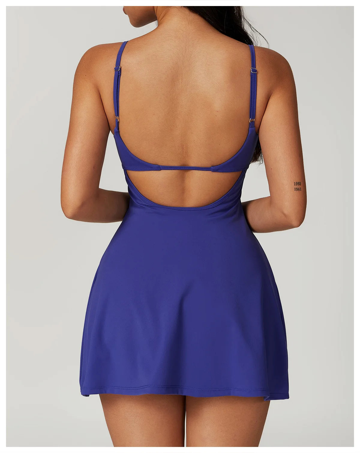 Back view of the Bree Yoga Dress in royal blue color. Shows the open-back design with thin adjustable straps crossing the back, A-line skirt falling to mini length. Photographed against a neutral background.