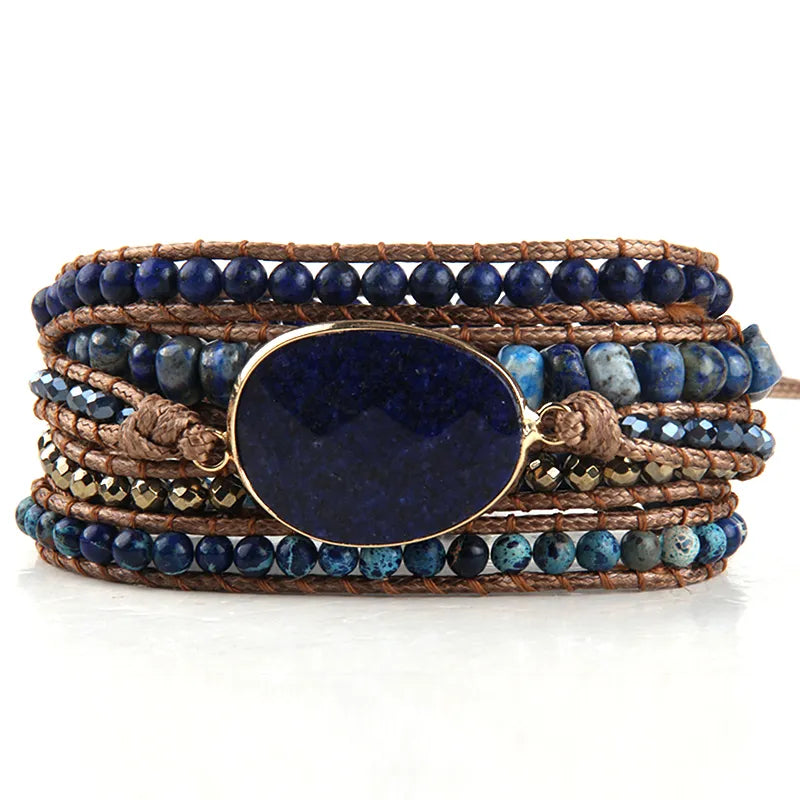 Navy blue Bohemian style wrap bracelet with a large center stone and several colorful smaller stones set in a natural cording. The bracelet rests on driftwood. Navy Boho Crystal Bracelet Set - Shop The Kei