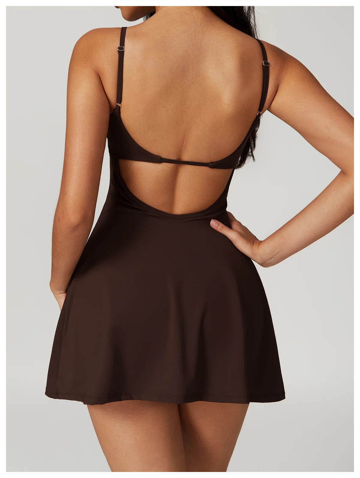 Back view of the Bree Yoga Dress in Espresso brown color. Shows the open-back design with thin adjustable straps crossing the back, A-line skirt falling to mini length. Photographed against a neutral background.