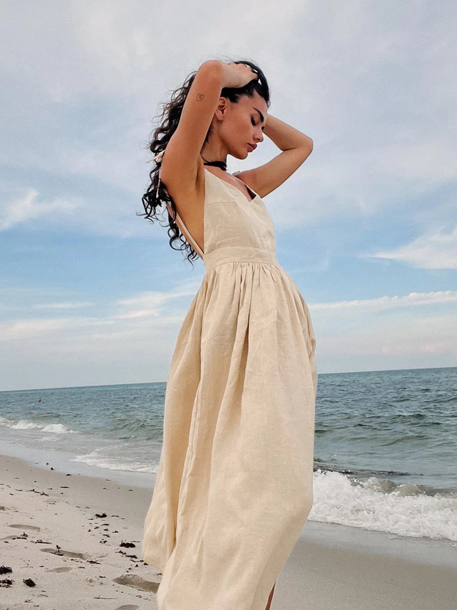 Isla Summer Dress from Shop the Kei - Natural linen dress with gathered waist, worn by a woman standing on the sand gazing peacefully at the shore.