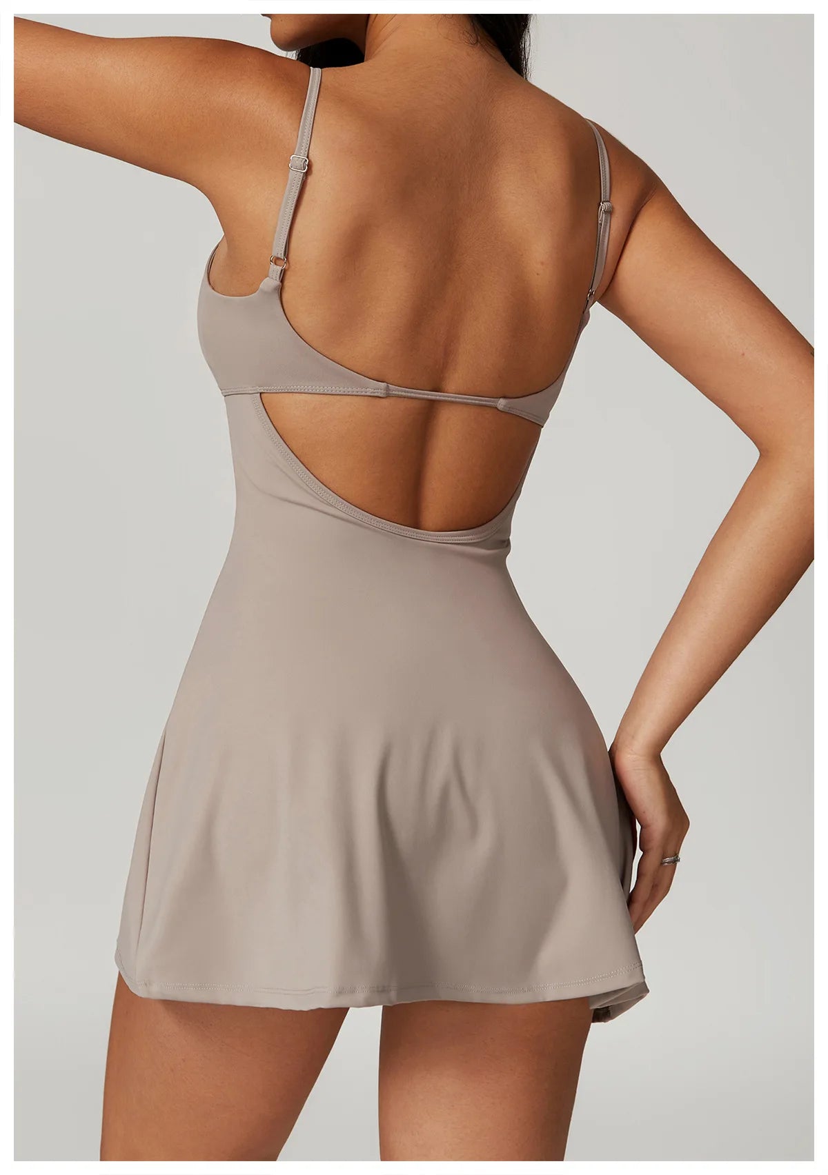 Back view of the Bree Yoga Dress in dark linen color. Shows the open-back design with thin adjustable straps crossing the back, A-line skirt falling to mini length. Photographed against a neutral background.