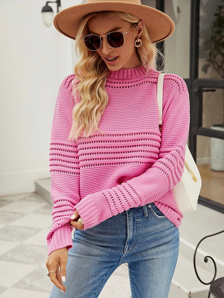 Lea Sweater from Shop the Kei - Model wearing a relaxed fit bright pink knitted sweater with horizontal openwork pattern detail and long sleeves, paired with light blue jeans. The model has long blonde hair and accessorizes with a wide-brimmed tan hat, round sunglasses, and a white leather crossbody bag. The outfit is styled for casual spring or summer wear, photographed outside a modern building with minimal architectural elements.
