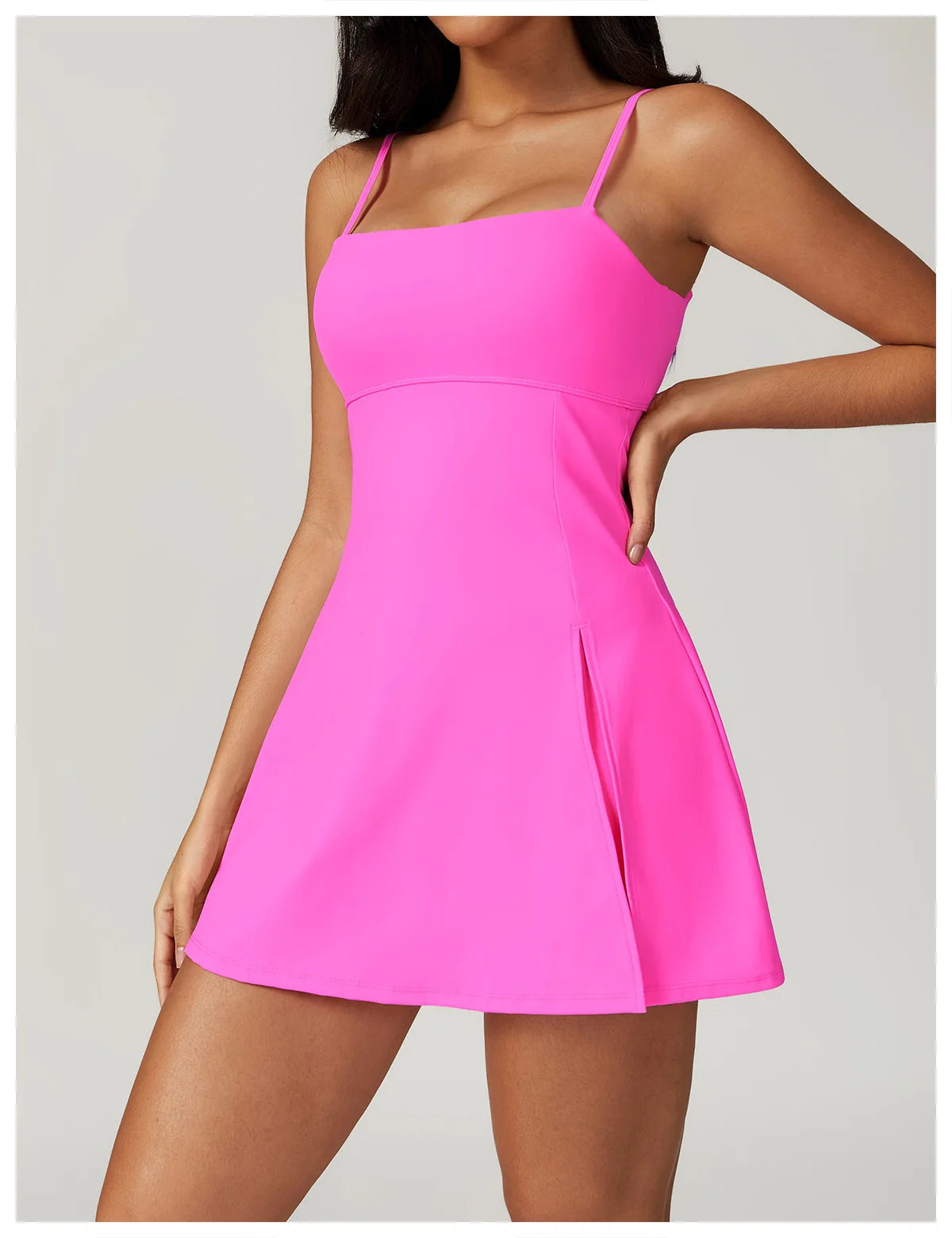 Close up view of the Bree Yoga Dress in pink color. Features thin spaghetti straps, straight neckline, fitted bodice, and A-line skirt with a pronounced side slit. Mini-length dress photographed against a neutral background.