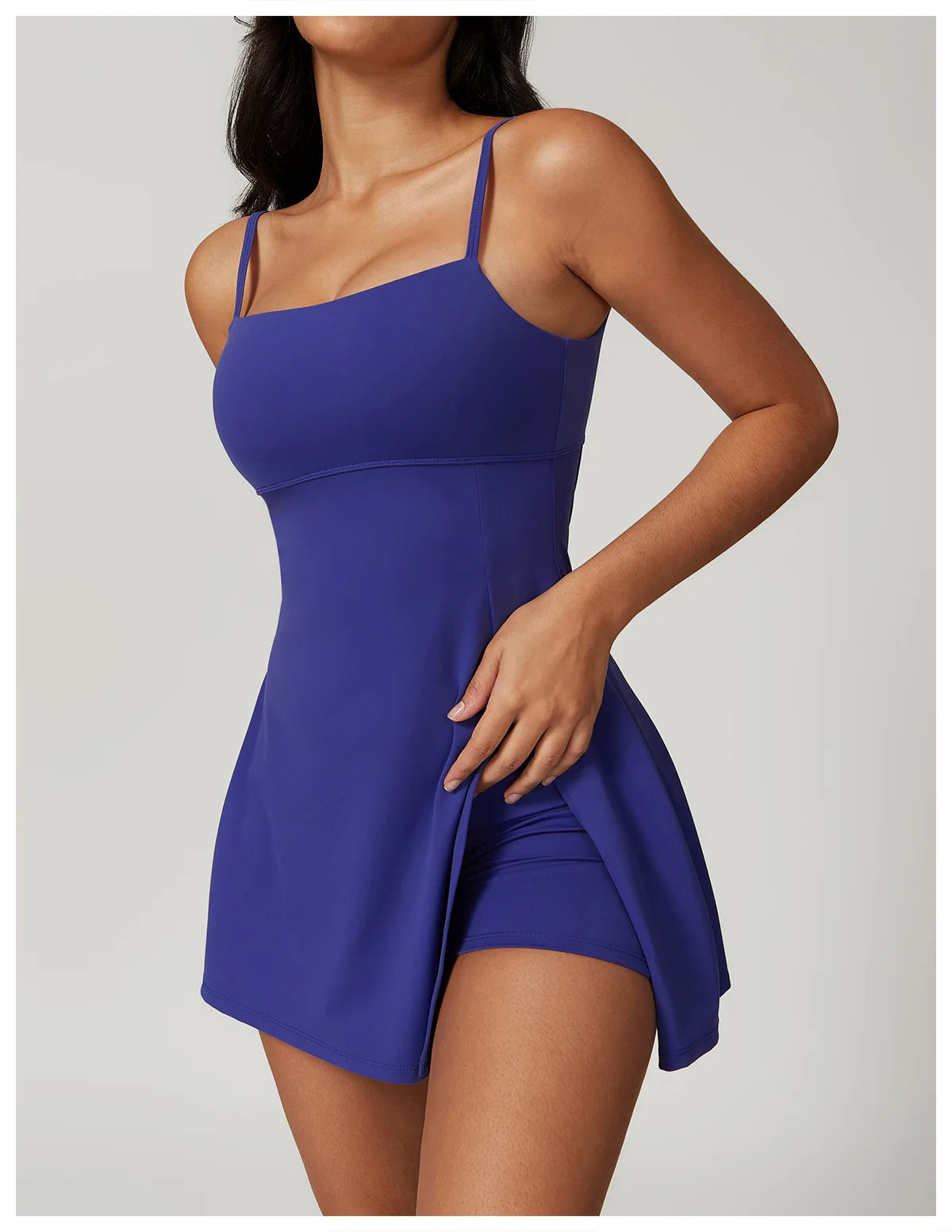 Close up view of the Bree Yoga Dress in blue color. Features thin spaghetti straps, straight neckline, fitted bodice, and A-line skirt with a pronounced side slit. Mini-length dress photographed against a neutral background.