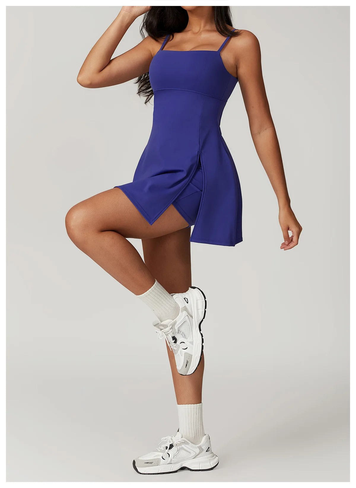 Front view of the Bree Yoga Dress in "Blue Glass" color. A mini dress with thin spaghetti straps, straight neckline, fitted bodice, and short A-line skirt. Model is in motion with white ankle socks and chunky athletic sneakers against a neutral background.