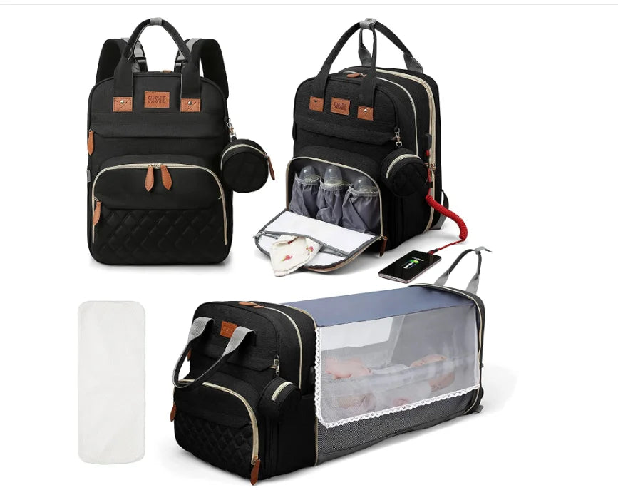 Black Lotus 3-in-1 Bassinet Diaper Bag backpack with orange leather accents, featuring quilted front pocket, dual carry handles, and small circular accessory pouch. Front of bag is displayed closed. A quarter turn of the bag reveals a thermal bottle pocket unzipped. Fully extended bassinet feature displayed with a baby inside