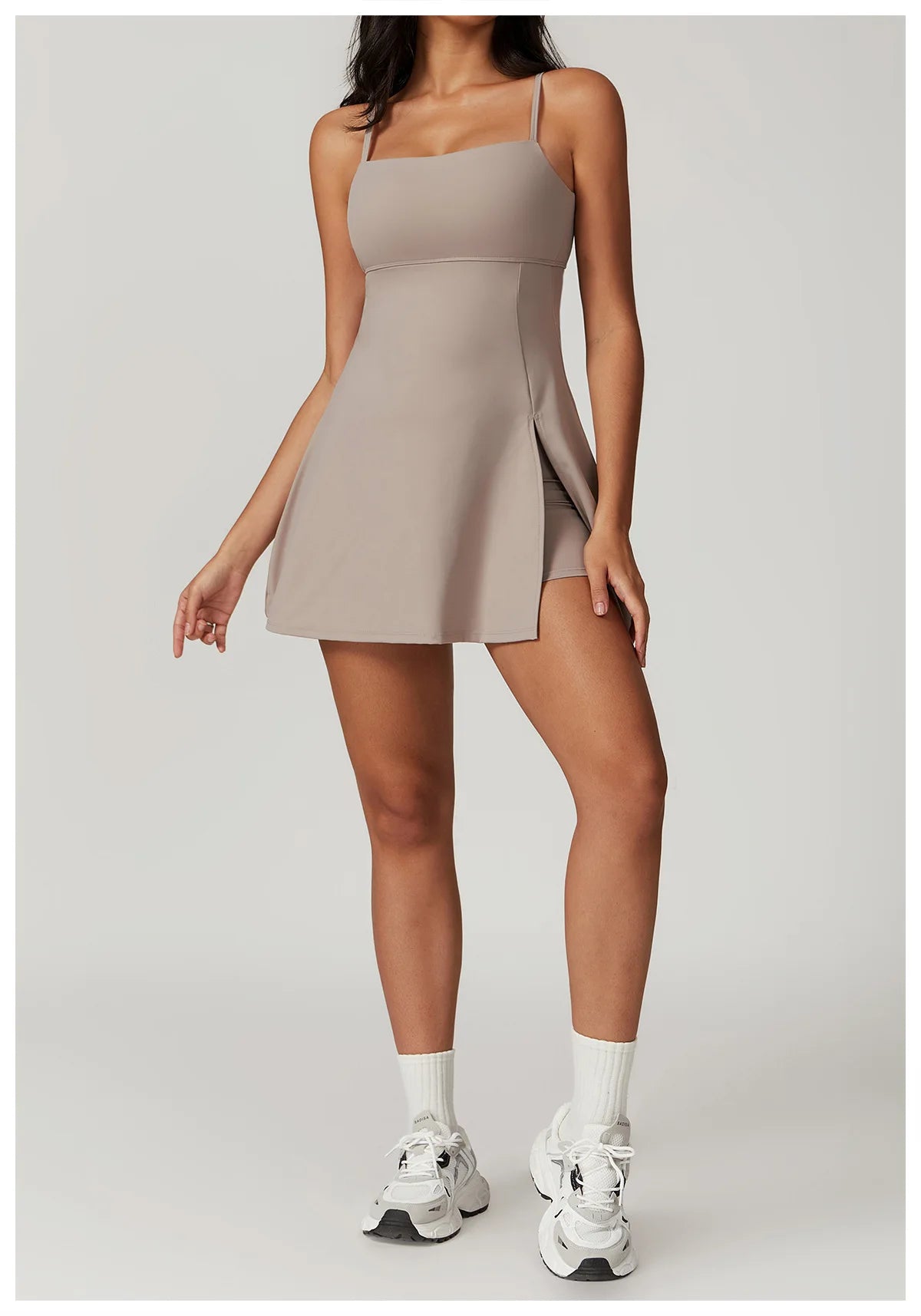 Front view of the Bree Yoga Dress in dark linen color. A mini dress with thin spaghetti straps, straight neckline, fitted bodice, and short A-line skirt. Model is in motion with white ankle socks and chunky athletic sneakers against a neutral background.