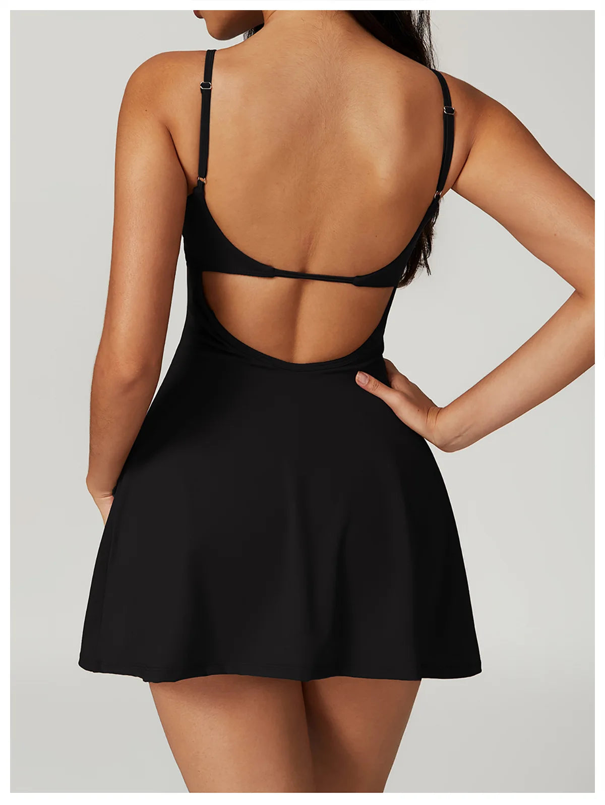 Back view of the Bree Yoga Dress in classic black color. Shows the open-back design with thin adjustable straps crossing the back, A-line skirt falling to mini length. Photographed against a neutral background.