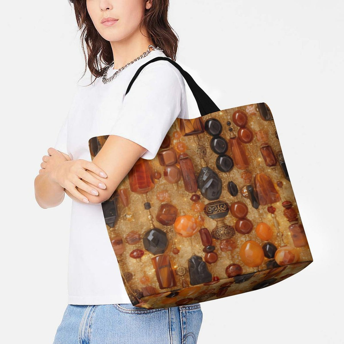 A woman wearing a white t-shirt and blue jeans carries a large tote bag over her shoulder. The tote bag features an artistic print of various polished gemstones and crystals in earthy tones of brown, orange, black, and beige on a textured background.