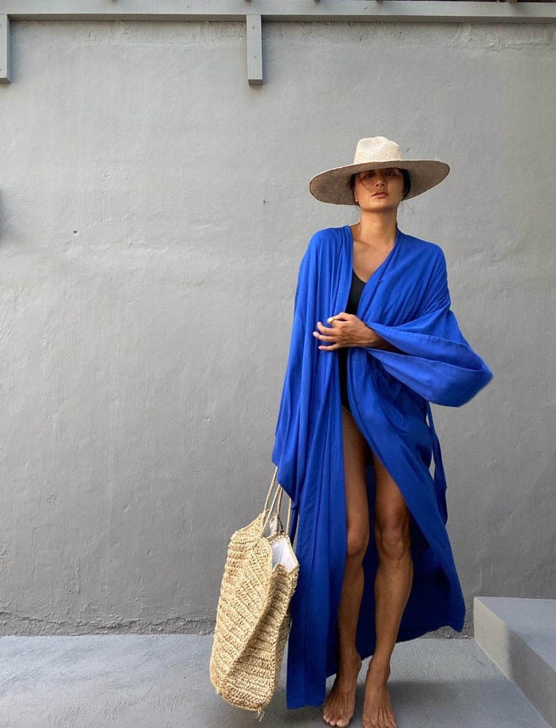 Front view of model wearing the royal blue Sole Kimono from Shop the Kei with a black swimsuit, straw hat, and beach tote. A Bohemian-style ankle-length beach cover-up kimono with wide sleeves and matching waist sash, perfect for vacation, poolside, or post-swim lounging.
