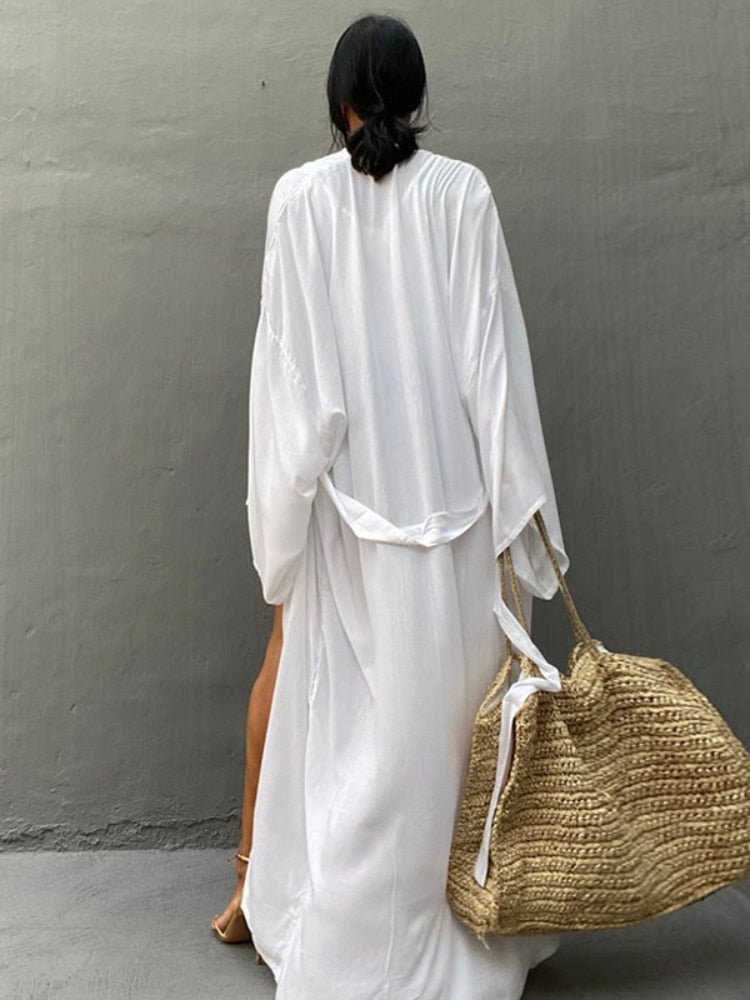 Back view of model wearing the white Sole Kimono from Shop the Kei with a beach tote. A Bohemian-style ankle-length beach cover-up kimono with wide sleeves and matching waist sash, perfect for vacation, poolside, or post-swim lounging.