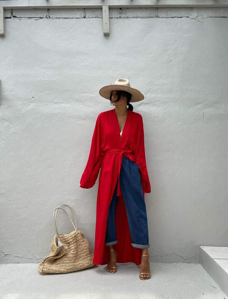 Front view of model wearing the red Sole Kimono from Shop the Kei tied at the waist with a white bikini top, baggy jeans, gold heels, straw hat and beach tote . A Bohemian-style ankle-length beach cover-up kimono with wide sleeves and matching waist sash, perfect for vacation, poolside, or post-swim lounging.