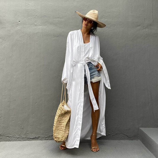 Front view of model wearing the white Sole Kimono from Shop the Kei with a white tank, denim shorts, straw hat, and beach tote. A Bohemian-style ankle-length beach cover-up kimono with wide sleeves and matching waist sash, perfect for vacation, poolside, or post-swim lounging.