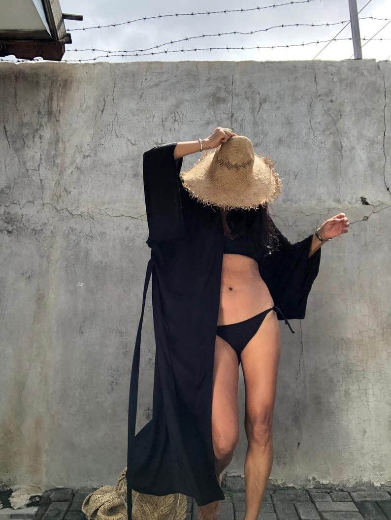 Front view of model wearing the black Sole Kimono from Shop the Kei with a black bikini and a straw hat. A Bohemian-style ankle-length beach cover-up kimono with wide sleeves and matching waist sash, perfect for vacation, poolside, or post-swim lounging.