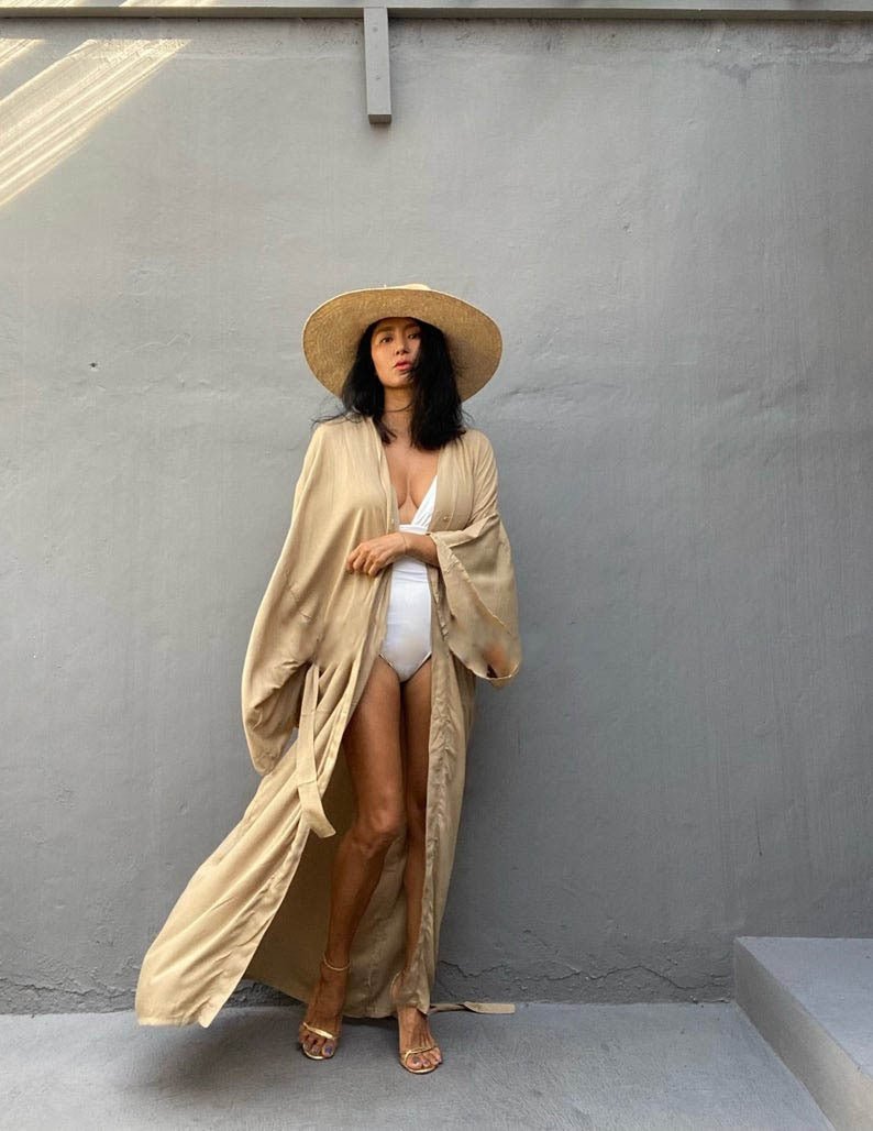 Front view of model wearing the Sand Sole Kimono from Shop the Kei with a white one piece swimsuit, straw hat, and gold heels. A Bohemian-style ankle-length beach cover-up kimono with wide sleeves and matching waist sash, perfect for vacation, poolside, or post-swim lounging.