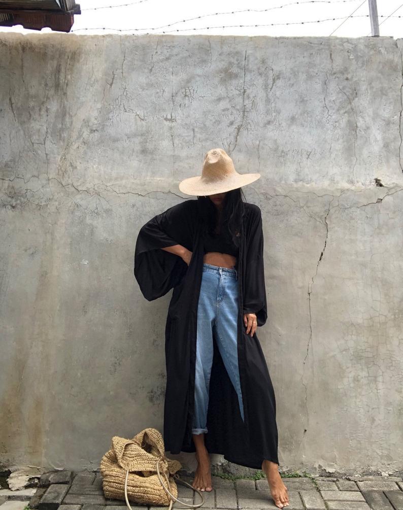 Front view of model wearing the black Sole Kimono from Shop the Kei with a black tank, baggy jeans, straw hat and beach tote . A Bohemian-style ankle-length beach cover-up kimono with wide sleeves and matching waist sash, perfect for vacation, poolside, or post-swim lounging.
