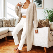 Woman wearing a beige cardigan over a white outfit in a living room setting.