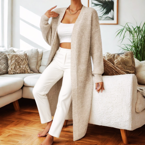 Woman wearing a beige cardigan over a white outfit in a living room setting.