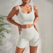 Model wearing Zen Yoga Shorts Set in white. Soft textured rib knit tank top with matching slim fit high waist shorts provide support and comfort during your movements. Model stands with hands on her hips in front of a white background.
