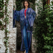 Woman wearing a blue floral kimono standing in a stone archway with greenery.