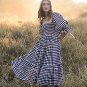 Front view of the Pixi Dress in black and white gingham pattern showcasing square neckline, voluminous puff sleeves, smocked bodice, and flowing tiered midi skirt. Dress photographed in a sunlit meadow