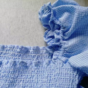 Close-up detail of the Pixi Dress showing sky blue gingham fabric with shirred bodice and decorative bow tie feature.