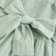 Close-up detail of the Pixi Dress showing light mint green gingham fabric with shirred bodice and decorative bow tie feature.