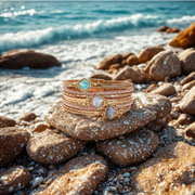 Stack of gold bracelets with gemstones on a rock by the ocean
