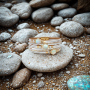 Stack of gold and white bracelets on a stone with pebbles in the background