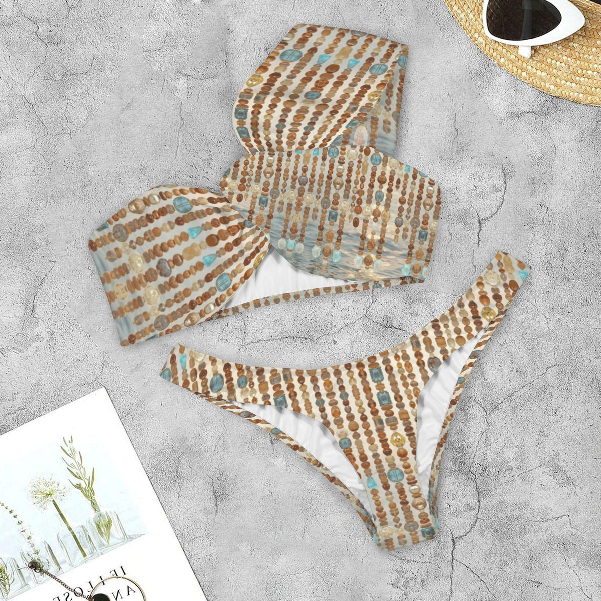 Water Goddess patterned bikini set on a textured surface with a magazine and sunglasses in the background.