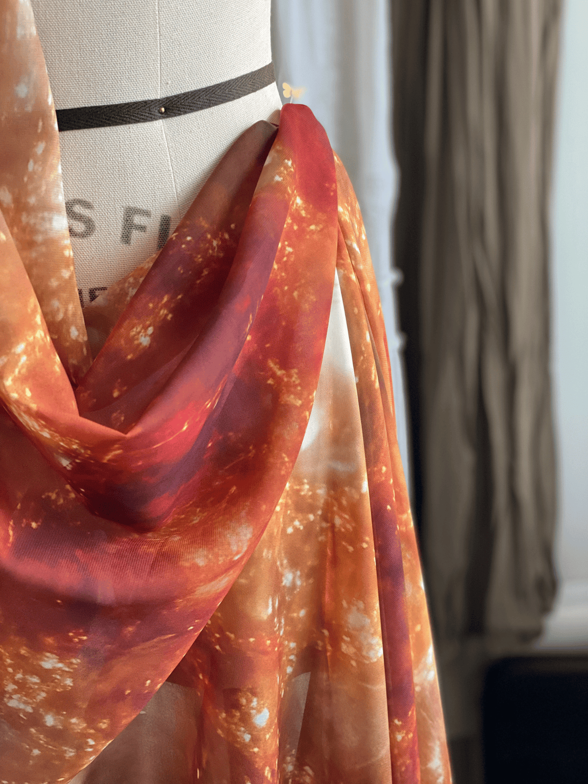 Close-up of a sheer orange fabric with a pattern draped over a mannequin.