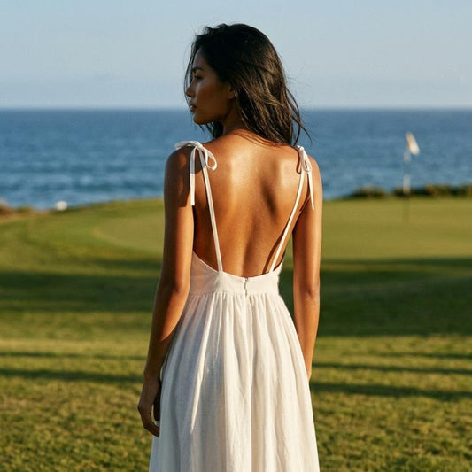 The open back view of a woman in a white dress standing on a golf course with ocean in the background