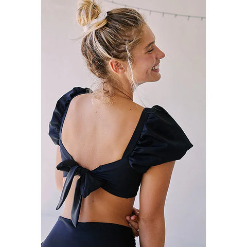 Back view of blonde model smiling in the black Lylah Bikini from ShoptheKei.com.  Top straps are tied into a bow, Low back neckline, and the high waist bikini bottom are visible.