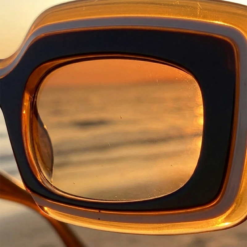 Extreme close-up looking through an amber-tinted Retro Shades lens at the ocean horizon during sunset.