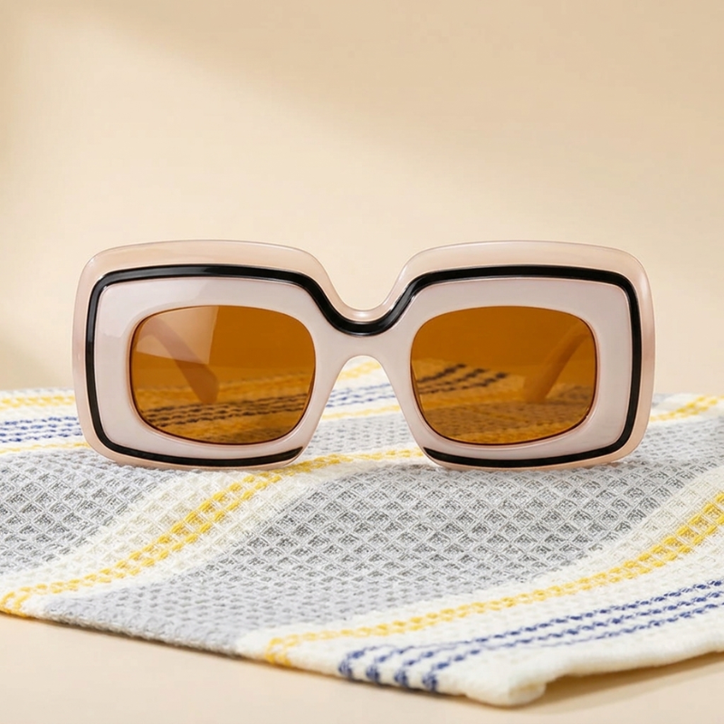 Champagne Retro Shades sunglasses, a cream and black frame with amber-tinted lenses, propped on a folded striped towel against a warm cream background.