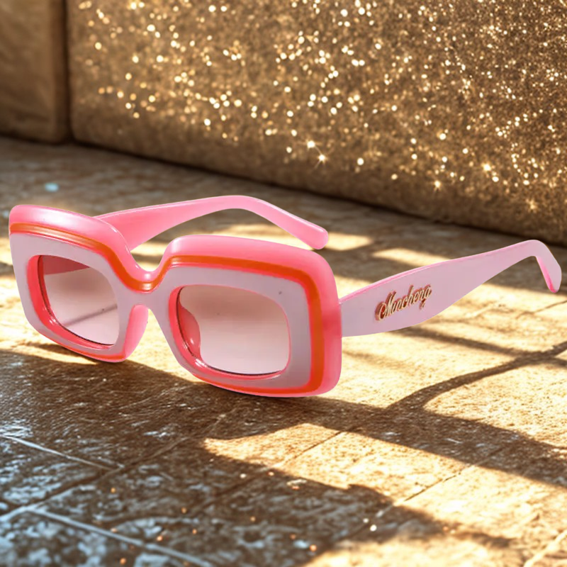Rose Quartz Retro Shades sunglasses resting on a sunlit tiled surface, styled in front of a sparkling gold glitter backdrop at golden hour.