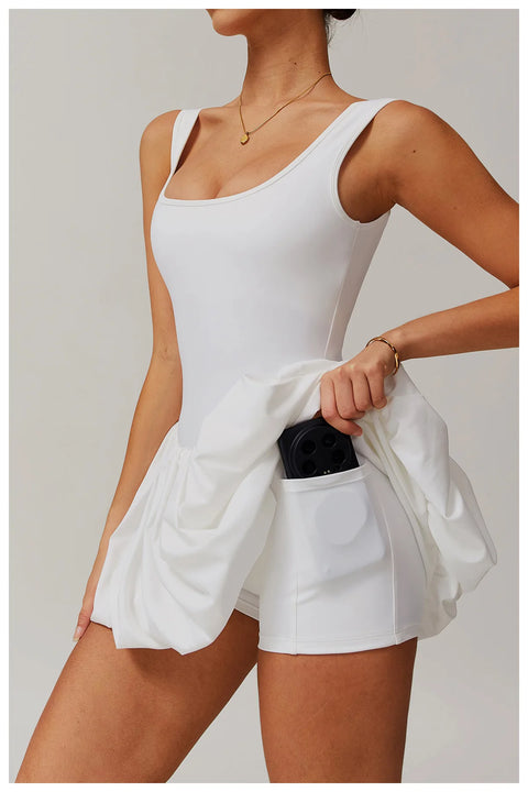 Side view of a model wearing the white Rinay Sport Dress from ShoptheKei activewear collection. Image reveals a pair of shorts sewn inside the dress and flat side pocket large enough for a phone or gym card.