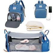 Blue baby diaper backpack shown in multiple views: with bottle storage compartment open, with USB charging port, folded mattress insert, and fully expanded as bassinet with mesh sides containing a baby. Lotus 3-in-1 bassinet diaper bag travel system with partial canopy
