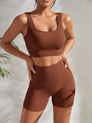 Model wearing Zen Yoga Shorts Set in Grounded brown. Soft textured rib knit tank top with matching slim fit high waist shorts provide support and comfort during your movements. Model stands with hands on her hips in front of a white background.