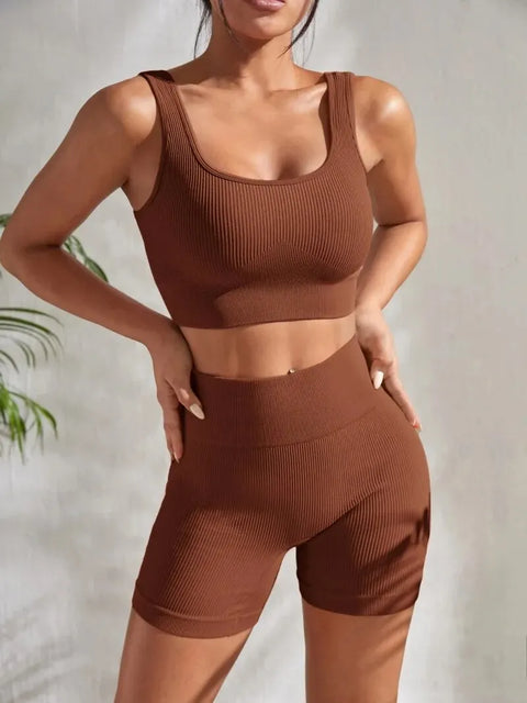 Model wearing Zen Yoga Shorts Set in Grounded brown. Soft textured rib knit tank top with matching slim fit high waist shorts provide support and comfort during your movements. Model stands with hands on her hips in front of a white background.