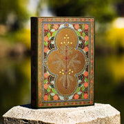 Decorative book with intricate designs on a stone surface with a blurred natural background