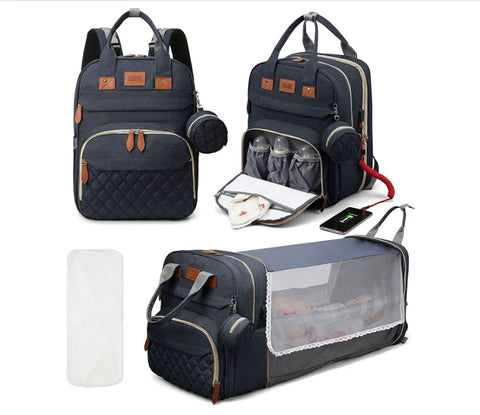 Dark Blue Lotus 3-in-1 Bassinet Diaper Bag backpack with orange leather accents, featuring quilted front pocket, dual carry handles, and small circular accessory pouch. Front of bag is displayed closed. A quarter turn of the bag reveals a thermal bottle pocket unzipped. Fully extended bassinet feature displayed with a baby inside