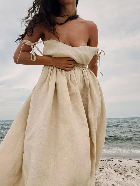 Isla Summer Dress from Shop the Kei -Close up of natural linen dress with gathered waist to show soft textile texture and fullness. Spaghetti straps elegantly drape off the shoulders and worn by a woman brunette waves softly swept up by a warm breeze on the beach