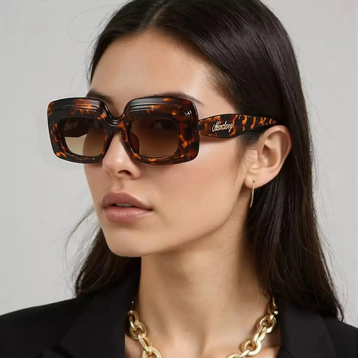 A model wearing Leopard Retro Shades sunglasses in a tortoiseshell pattern with brown gradient lenses, styled with a black blazer and a chunky gold chain necklace.
