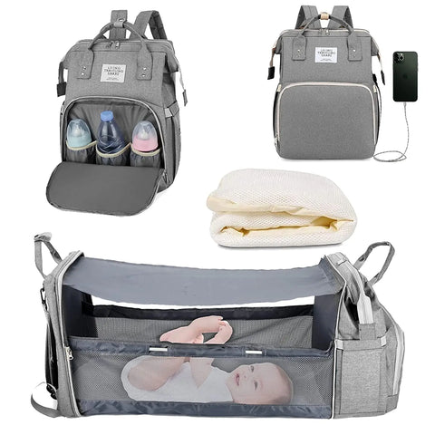 Gray baby diaper backpack shown in multiple views: with bottle storage compartment open, with USB charging port, folded mattress insert, and fully expanded as bassinet with mesh sides containing a baby. Lotus 3-in-1 bassinet diaper bag travel system with partial canopy